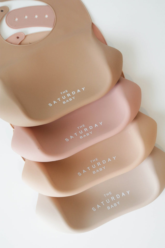 a set of three pink and beige bibs with the words saturday on them